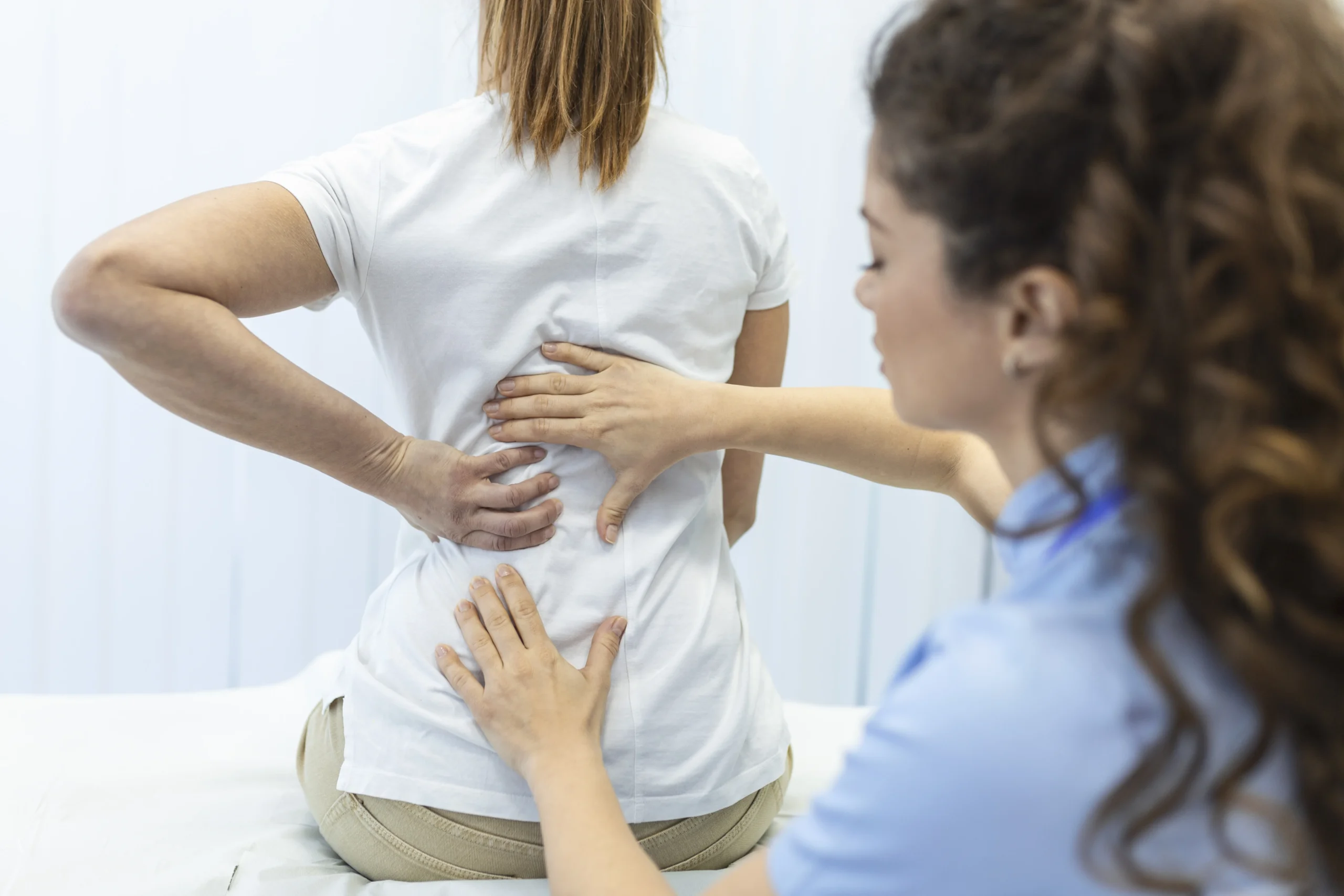 Physical therapist providing back pain treatment and spinal assessment for a patient during a rehabilitation session.