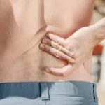A man holding his lower back in pain, highlighting discomfort associated with potential tendon and ligament injuries.