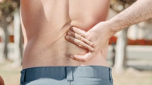 A man holding his lower back in pain, highlighting discomfort associated with potential tendon and ligament injuries.