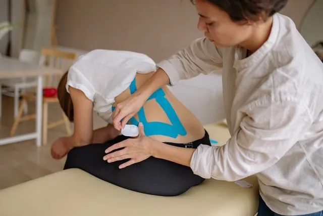 A physiotherapist applying kinesiology tape to a patient's back as part of non-surgical back pain treatment.