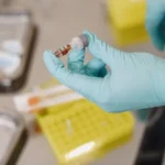 A healthcare professional wearing blue gloves holding a vial of blood sample for PRP and stem cell therapy preparation.