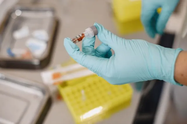 A healthcare professional wearing blue gloves holding a vial of blood sample for PRP and stem cell therapy preparation.